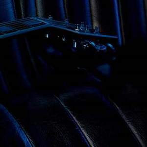 A close-up view of a sleek electric guitar resting on a dark textured surface, with a stylish fragrance bottle placed at an angle on the guitar. The overall color scheme features deep blues and blacks, creating an elegant atmosphere.