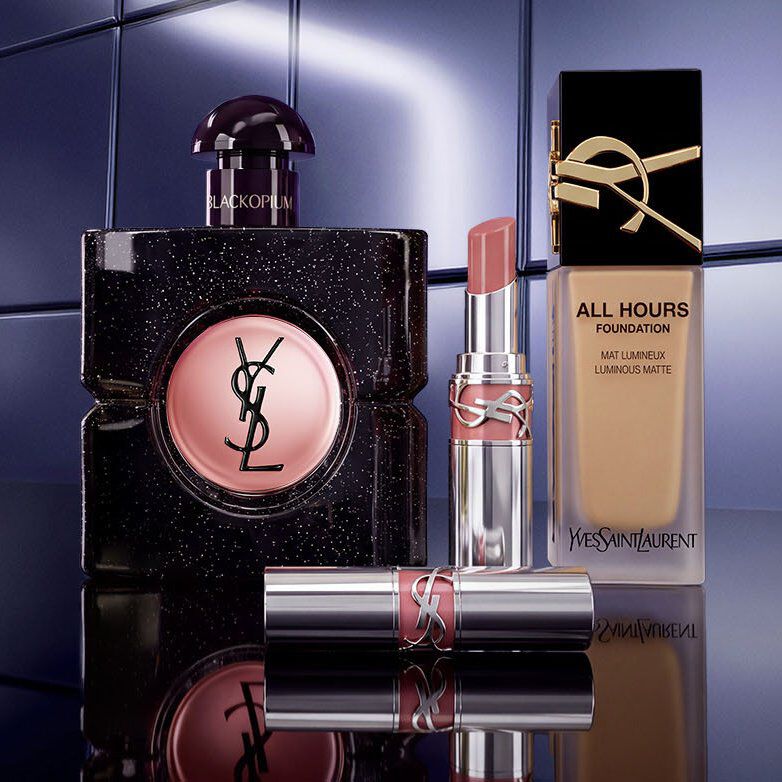 Estuches de regalo de la coleccion navidena de Yves Saint Laurent y productos de belleza de lujo sobre fondo rojo festivo.