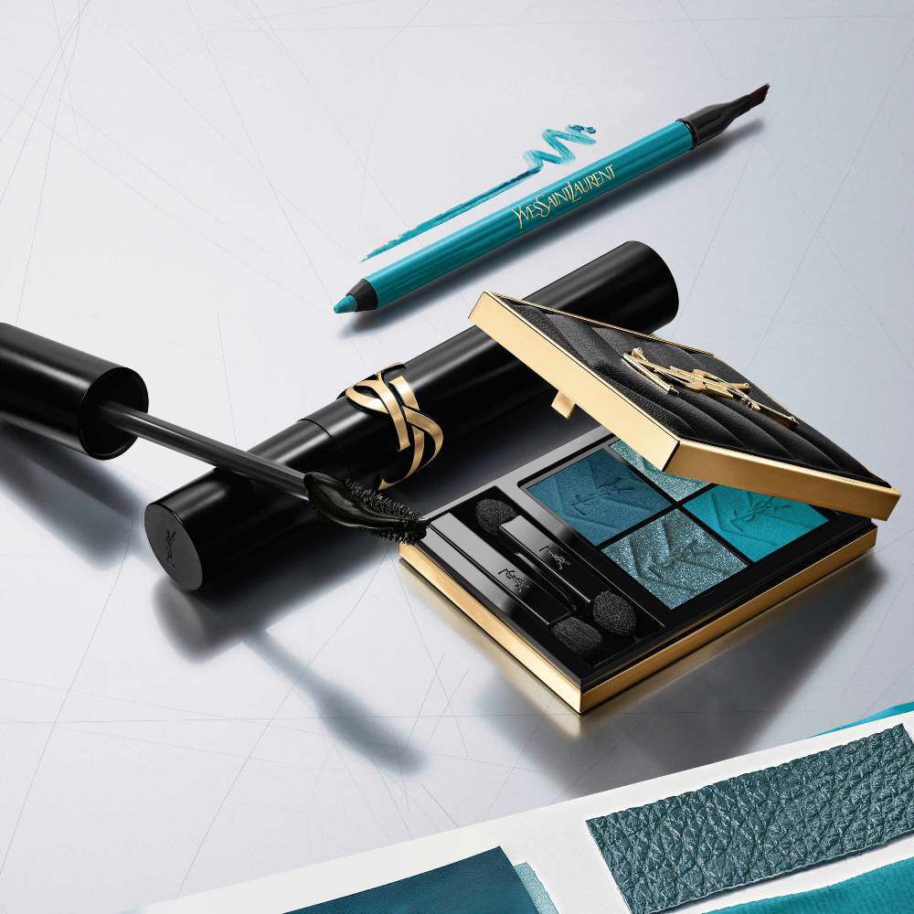 Coleccion de maquillaje de lujo YSL: paleta de sombras azul, mascara de pestanas y delineador sobre fondo plateado.