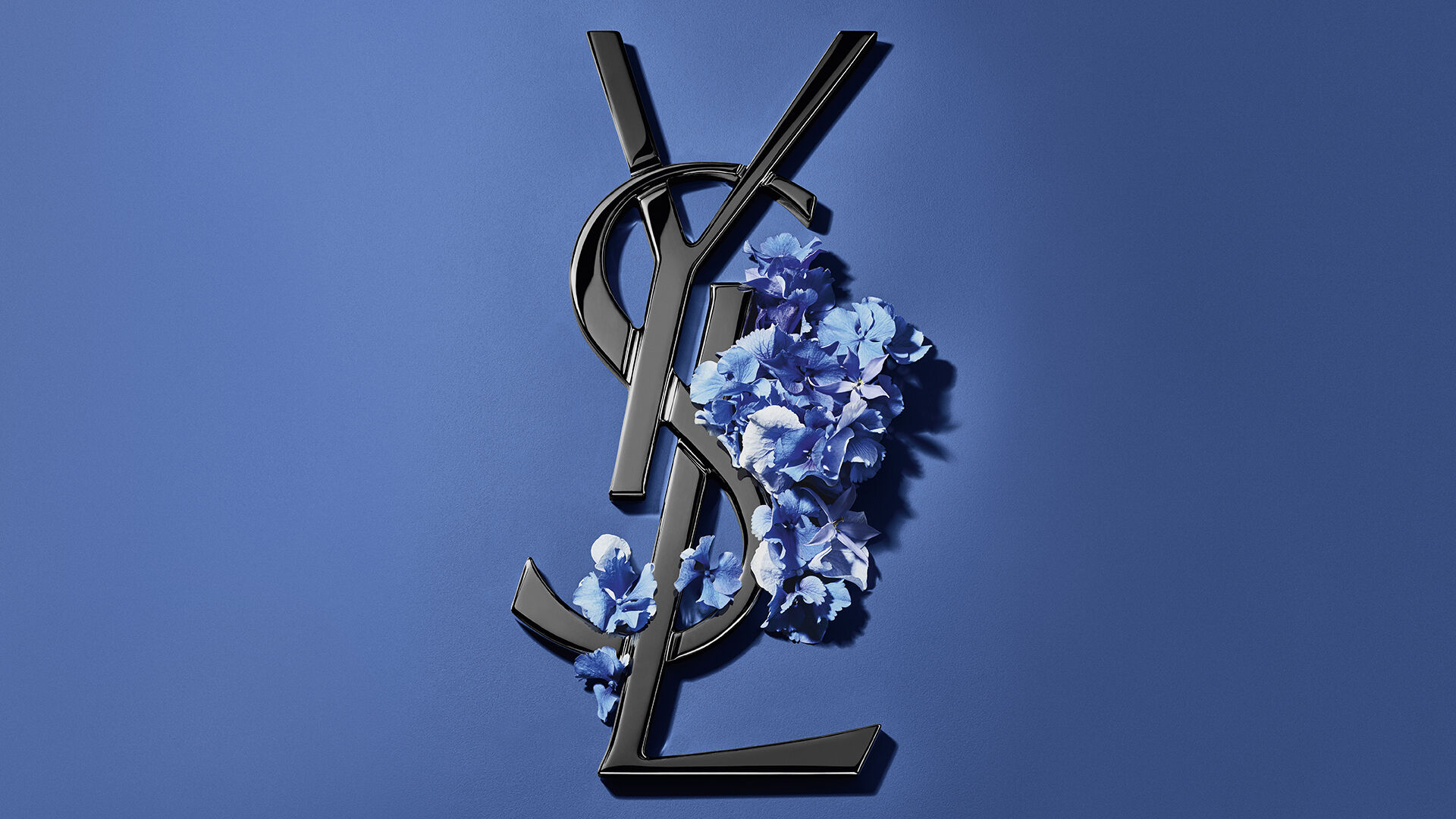 Caja de regalo YSL azul rodeada de hortensias sobre fondo azul.