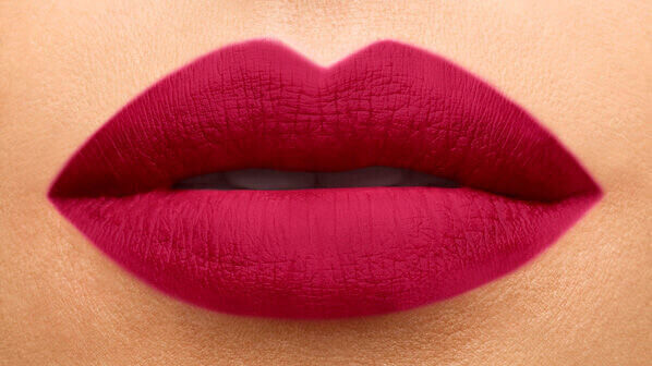 Close-up of a pair of lips elegantly painted in a dark magenta lipstick shade, showcasing a smooth matte finish.