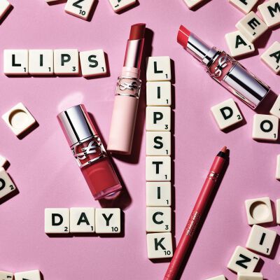 Labiales YSL y lapiz de labios sobre fondo rosa con letras de Scrabble que forman las palabras "LIPS", "LIPSTICK" y "DAY"