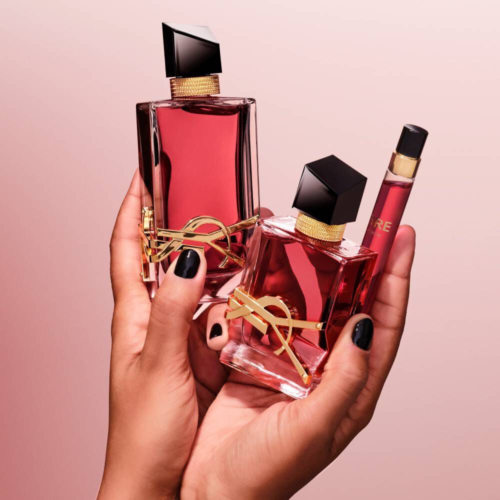 Manos sosteniendo dos frascos de perfume YSL rojos y un spray de viaje