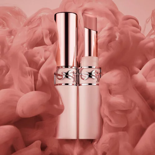 Dos barras de labios en oro rosa sobre un fondo rosa con efecto humo.