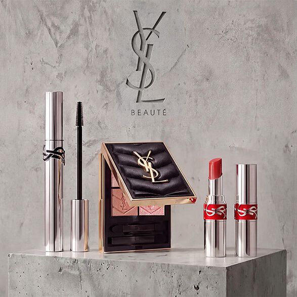 Exposicion promocional de productos de maquillaje de YSL Beaute que incluye mascara de pestanas, una paleta de sombras de ojos acolchada y pintalabios sobre un fondo de hormigon.