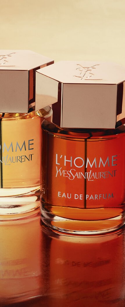 Cuatro frascos de perfume de Yves Saint Laurent sobre una superficie brillante, con diferentes tonos de liquido en cada botella.