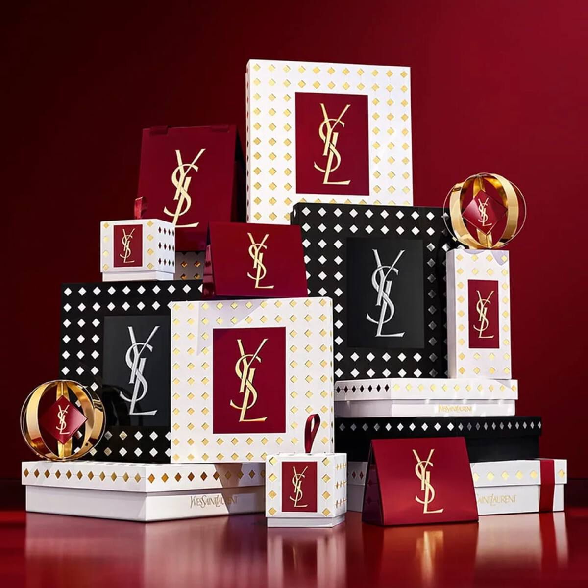 Estuches de regalo de la coleccion navidena de Yves Saint Laurent y productos de belleza de lujo sobre fondo rojo festivo.
