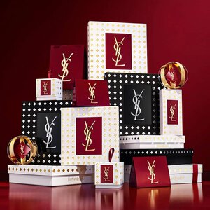 Estuches de regalo de la coleccion navidena de Yves Saint Laurent y productos de belleza de lujo sobre fondo rojo festivo.