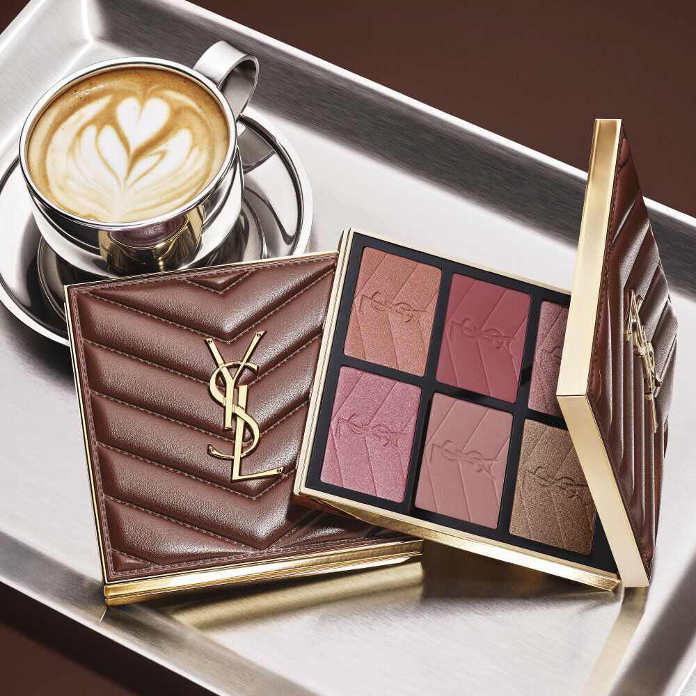 Paleta de maquillaje YSL y bolso acolchado junto a un cafe sobre una bandeja plateada.