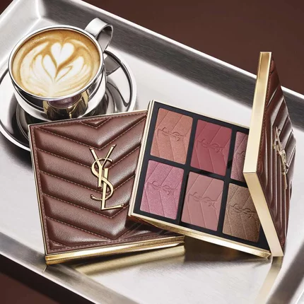 Paleta de maquillaje YSL y bolso acolchado junto a un cafe sobre una bandeja plateada.