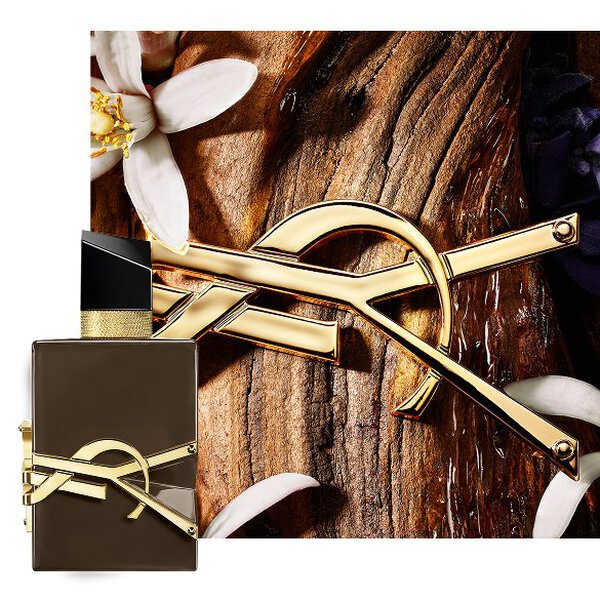 Frasco marron lacado Libre Santal Couture sobre corteza de sandalo, con Cassandre dorada y flores blancas.