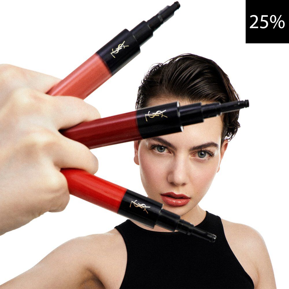 Una imagen de primer plano con una modelo mirando al frente, con una mano sosteniendo tres productos labiales liquidos de YSL en tonos rojos y coral. Un cuadro negro con el texto blanco '25%' es visible en la esquina superior derecha, indicando un descuento.