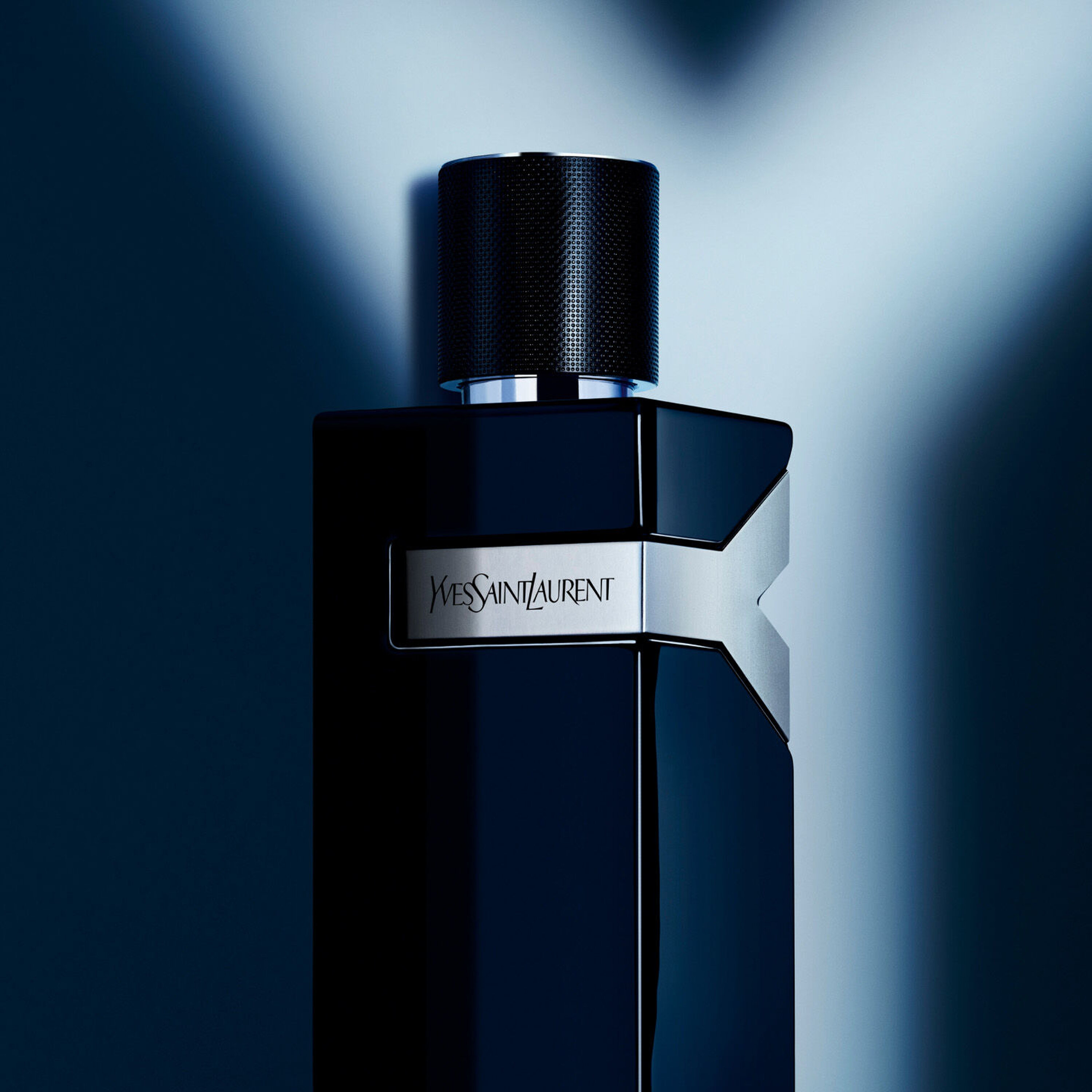A sleek, dark perfume bottle with a metallic label displaying "Yves Saint Laurent," set against a soft, shadowy background.