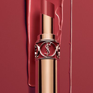A close-up of a gold lipstick tube against a rich red background. The lipstick has an elegant design, emphasizing luxury and beauty.