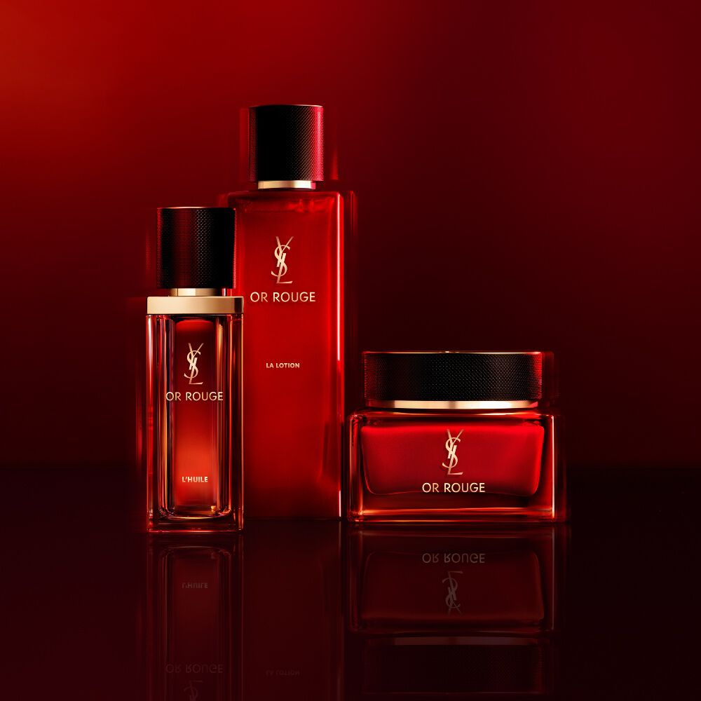 Tres productos de cuidado de la piel Yves Saint Laurent Or Rouge en frascos y tarro de vidrio rojo translucido sobre un fondo rojo oscuro.