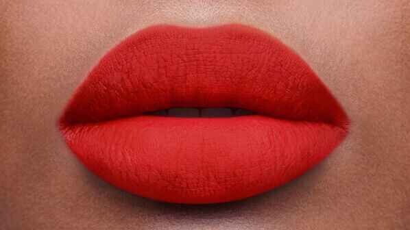 Close-up of a pair of full lips coated in bright red matte lipstick against a smooth skin backdrop.