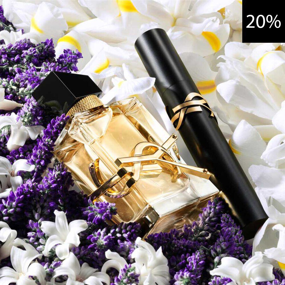 Un primer plano de un elegante frasco de perfume YSL Libre y un rimel YSL negro, ambos con detalles dorados, colocados entre vibrante lavanda morada y delicadas flores blancas y amarillas. Un cuadro negro con el texto blanco '20%' es visible en la esquina superior derecha, indicando un descuento.