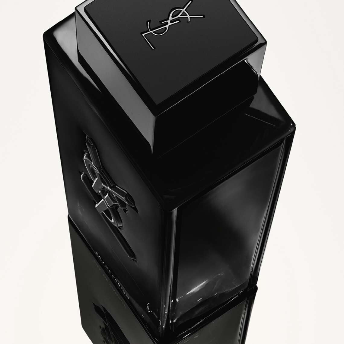 A sleek black fragrance bottle with a glossy finish, featuring a minimalist design and the YSL logo on the front and top. The bottle is set against a light background, creating a reflective effect.