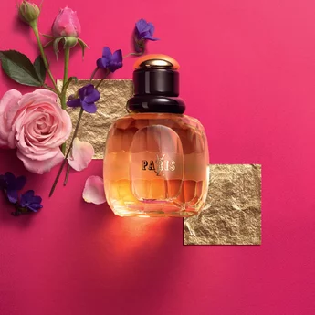 A stylish perfume bottle labeled "Paris" surrounded by pink roses and violets on a bright pink background, with gold geometric shapes accentuating the composition.