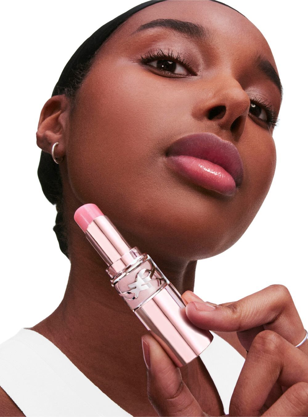 A close-up of a woman holding a lipstick, displaying a soft pink shade. She has a natural makeup look and is looking at the camera with a confident expression.