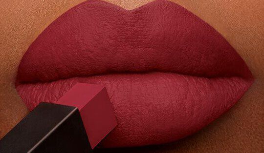 Close-up of a pair of full lips being applied with a deep red lipstick.