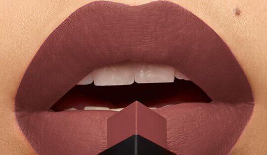 Close-up of a pair of lips wearing a matte mauve lipstick, with a lipstick bullet positioned at the center.