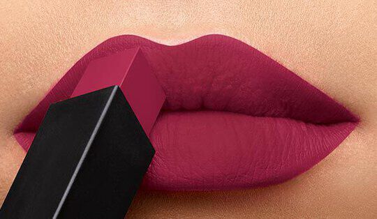 A close-up of lips wearing a deep magenta lipstick, with a lipstick tube positioned against them.