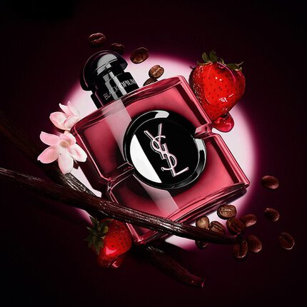 Frasco de perfume YSL Black Opium rodeado de granos de cafe, fresas, vainilla y flores blancas sobre fondo oscuro.