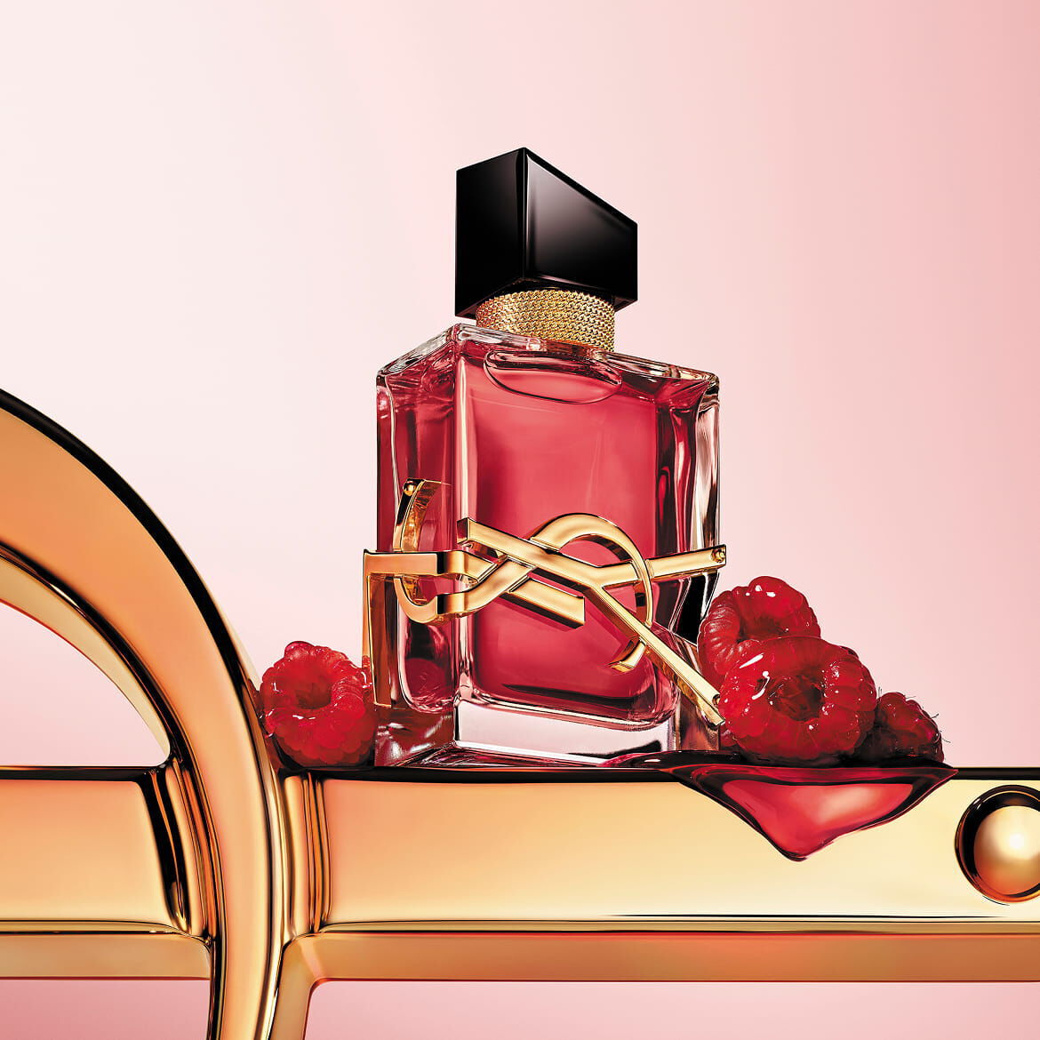 El frasco escarlata de YSL LIBRE Berry Crush, con su esencia vibrante, reposa sobre un majestuoso logo dorado, rodeado de frambuesas suculentas, prometiendo una firma audaz e irresistible.​