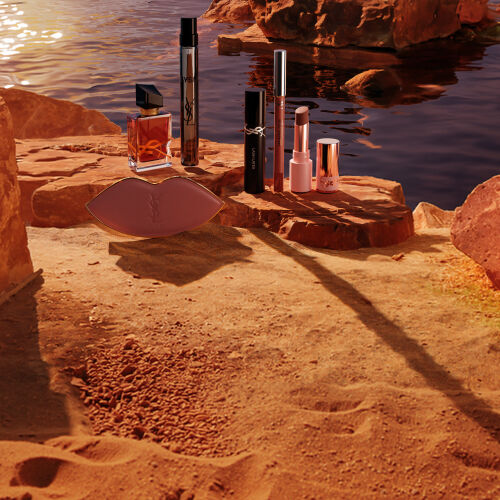 Maquillaje, perfumes YSL y neceser blanco en un desierto soleado.
