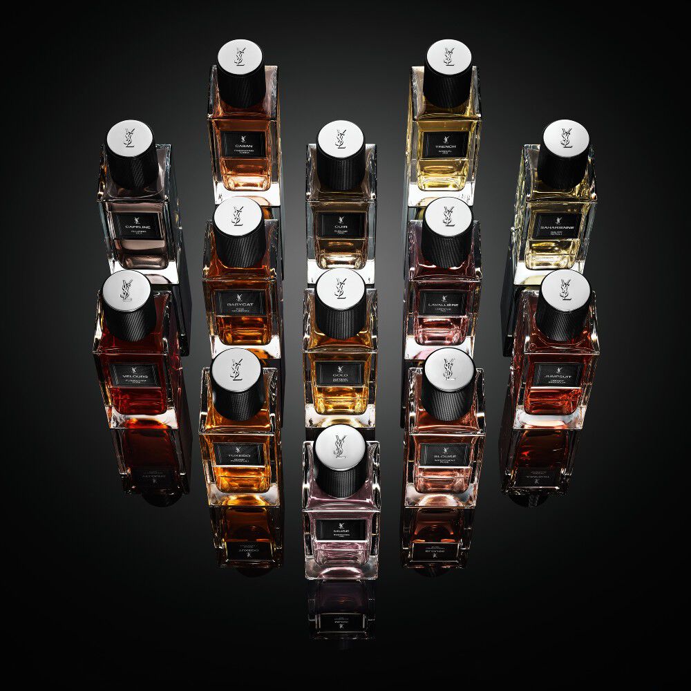 Una coleccion de frascos de la fragancia "Le Vestiaire des Parfums" de Yves Saint Laurent dispuestos en forma de diamante sobre una superficie negra reflectante.