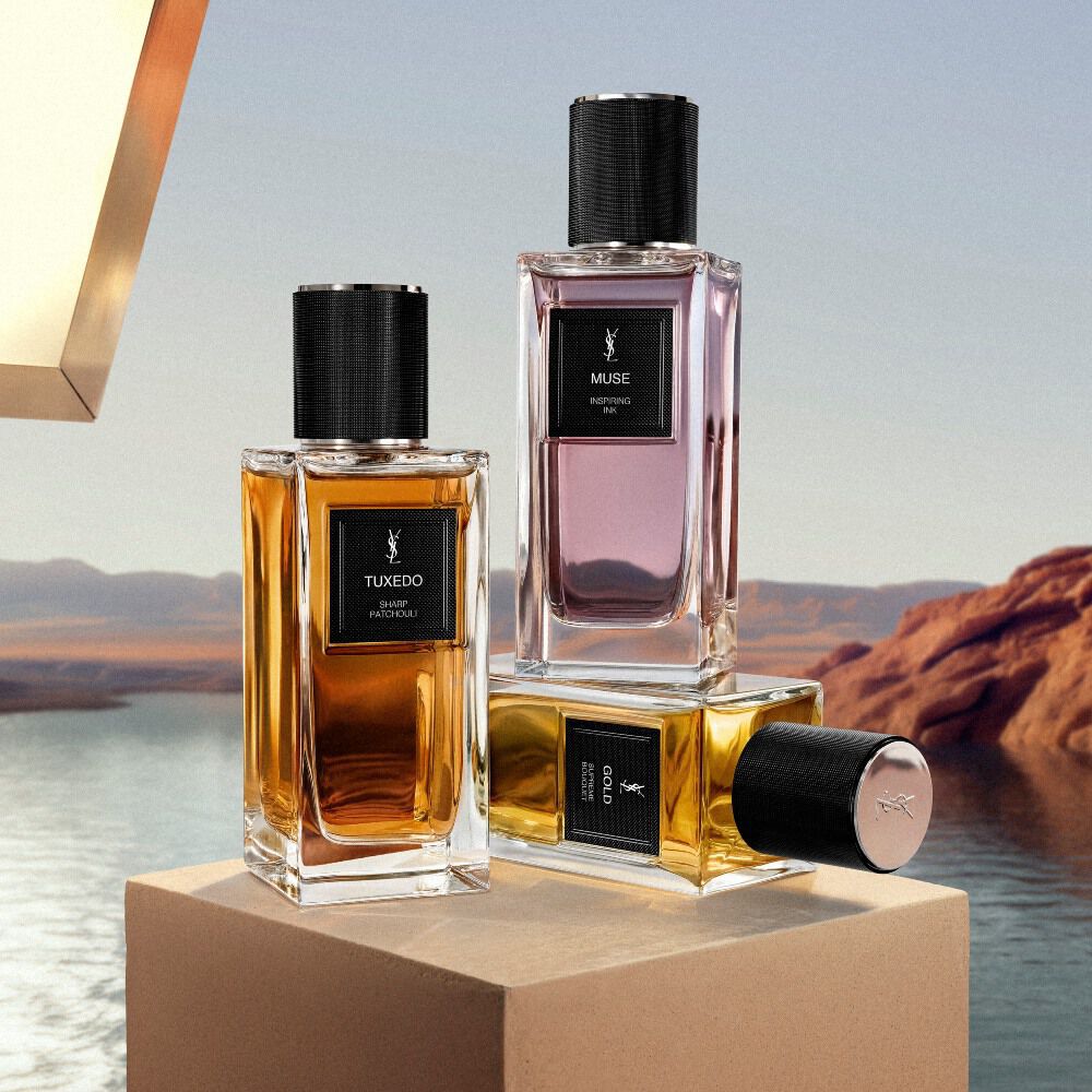 Frascos de YSL Le Vestiaire des Parfums expuestos sobre un pedestal junto a un lago desertico.