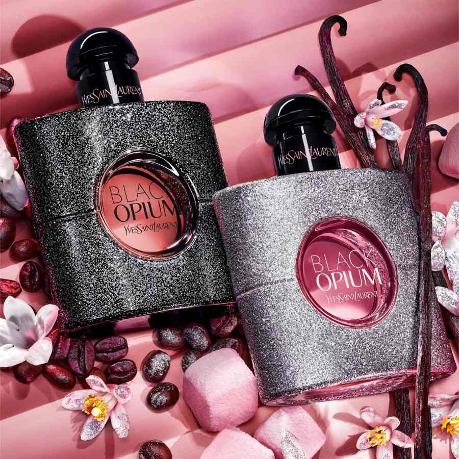 Dos frascos de YSL Black Opium sobre fondo rosa con flores y granos de cafe