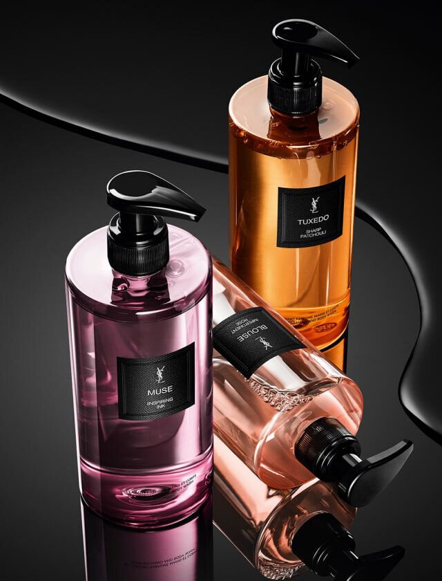 Three stylish bottles of liquid soap are arranged artistically on a reflective black surface, featuring pink, orange, and beige hues against a dark background.