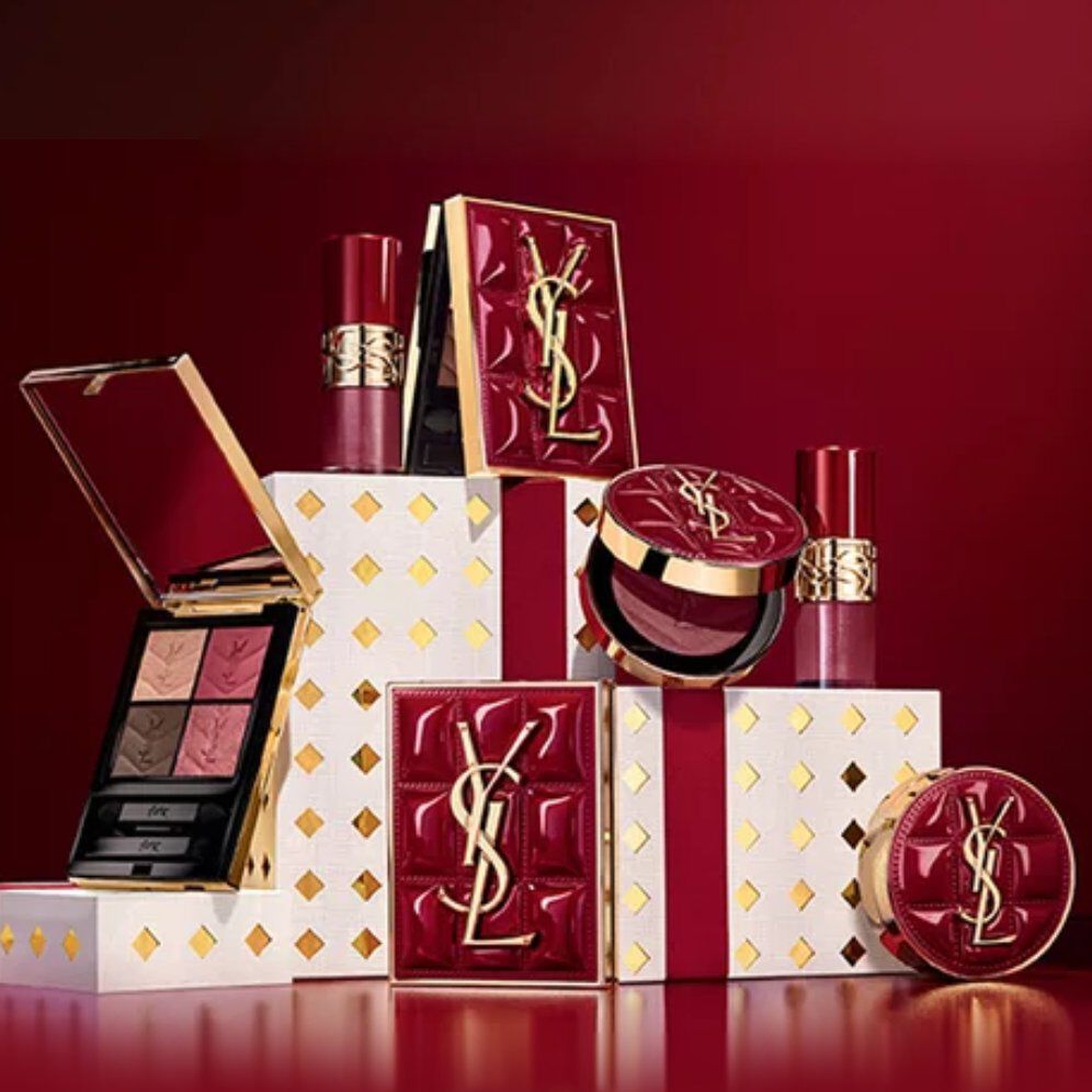 Estuches de regalo de la coleccion navidena de Yves Saint Laurent y productos de belleza de lujo sobre fondo rojo festivo.