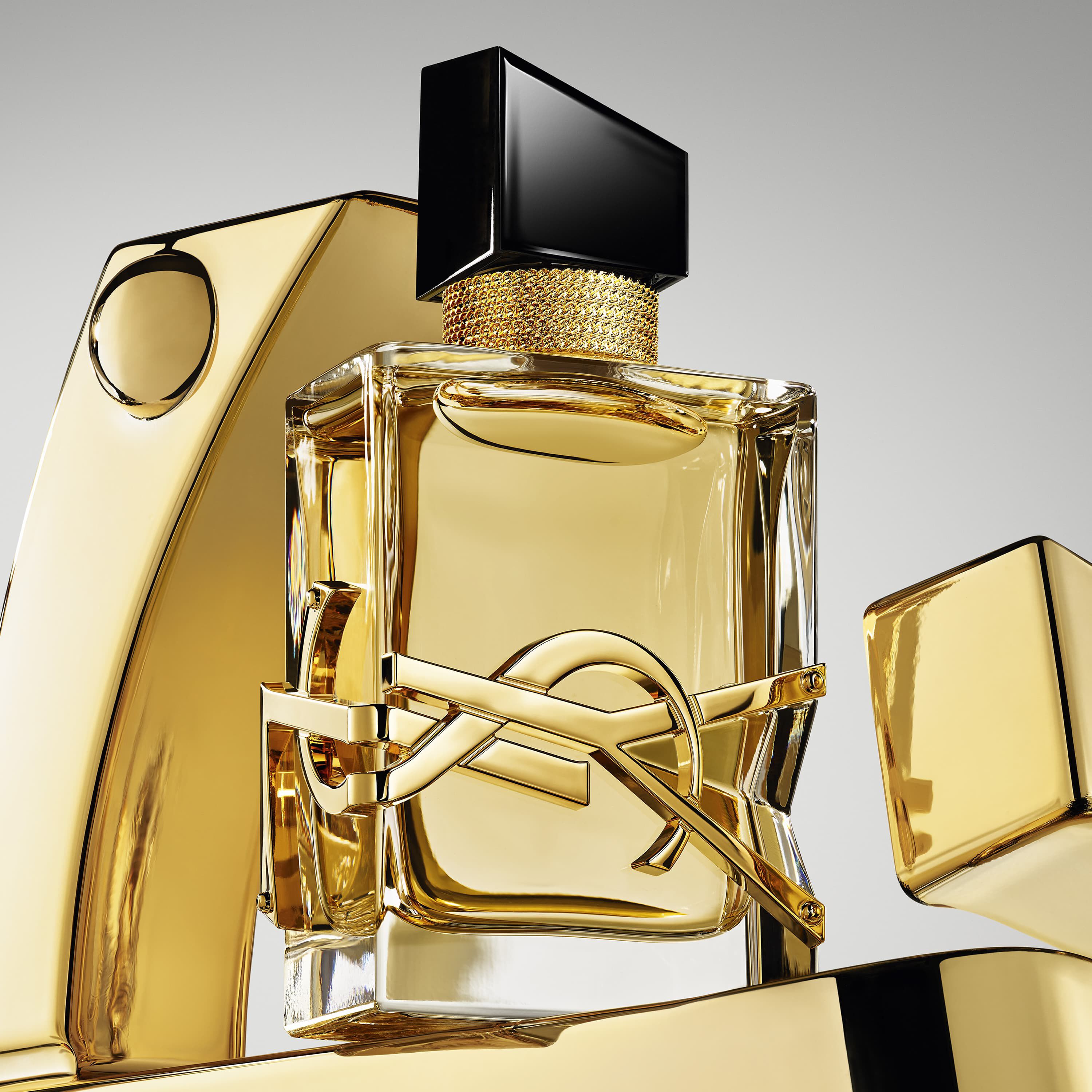 Frasco de perfume YSL dorado con tapa negra y logo, rodeado de elementos dorados.