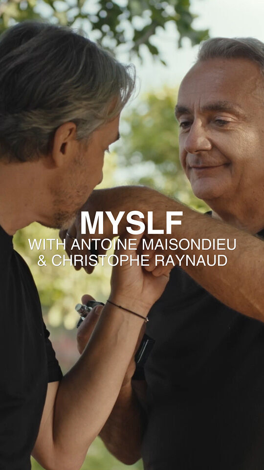 Dos hombres con camisetas negras interactuan al aire libre, uno de ellos sujetando el brazo del otro y un pequeno objeto. En la imagen aparece el texto "MYSLF WITH ANTOINE MAISONDIEU & CHRISTOPHE RAYNAUD" sobre un fondo borroso de follaje verde.