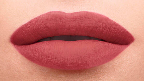 Close-up of a pair of lips with a matte, soft pink lipstick. The lips are slightly parted, showing a smooth texture.