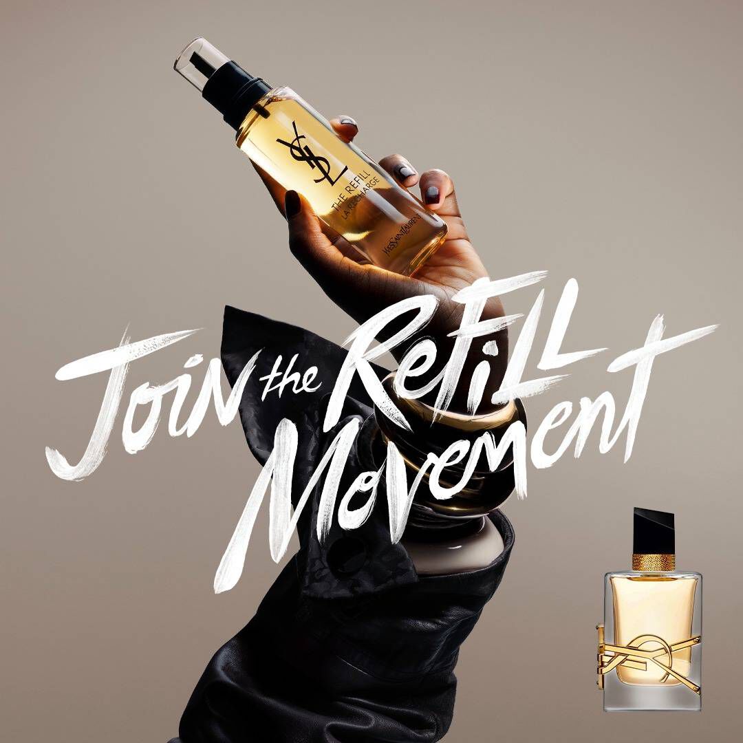 Una mano sostiene un frasco de recambio dorado sobre un fondo neutro. A la izquierda, un texto blanco de estilo pincel dice "Unete al movimiento REFILL" y a la derecha se muestra un frasco de fragancia de cristal clasico de YSL Libre con su caracteristico logotipo dorado.