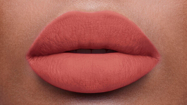 Close-up of a pair of plump, matte lips in a warm peachy tone.