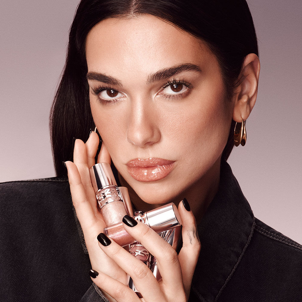 Dua Lipa, YSL Beauty ambassador, holding two YSL LOVESHINE Plumping Lip Oil Glosses, with a subtle gradient background.