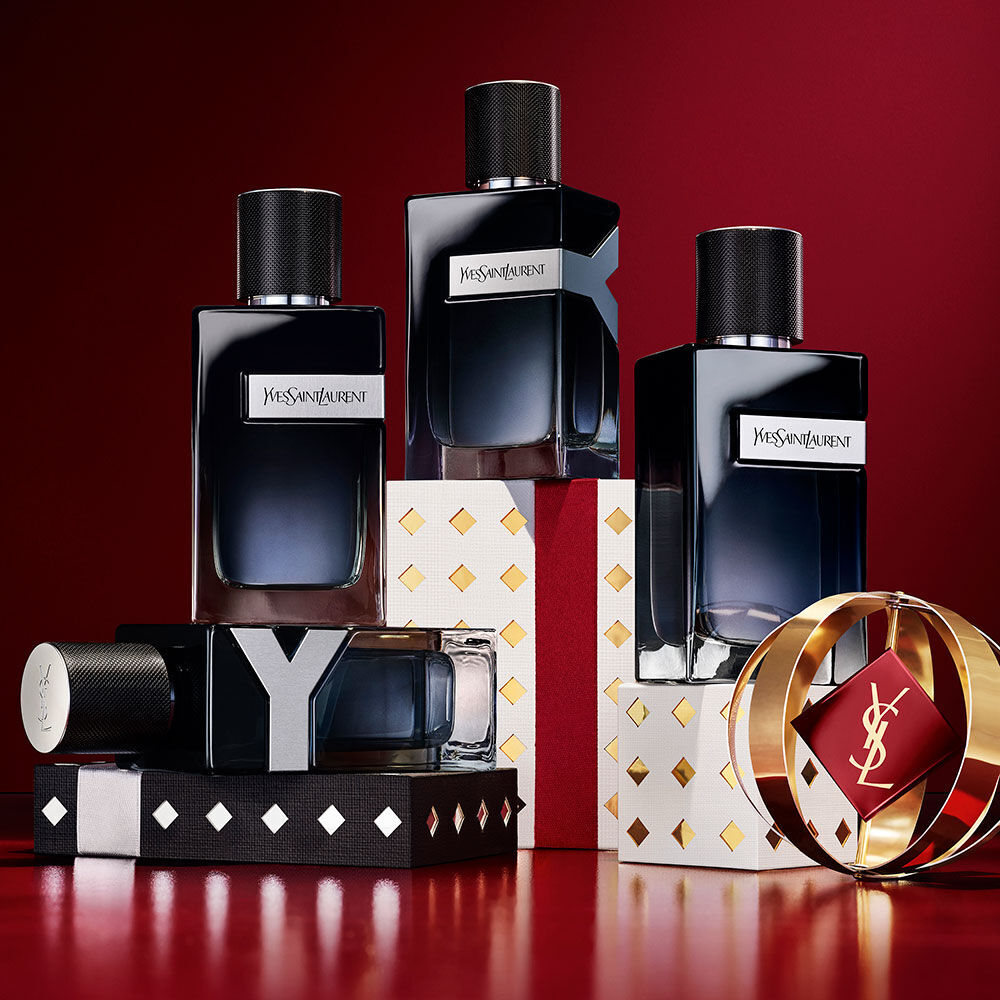 Frascos de YSL Y Eau de Parfum apilados sobre cajas navidenas en negro, blanco y oro.