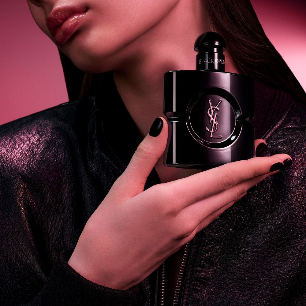 Frasco de Black Opium Le Parfum en negro brillante, rodeado de vainas de vainilla oscura y jazmin blanco con declaraciones.