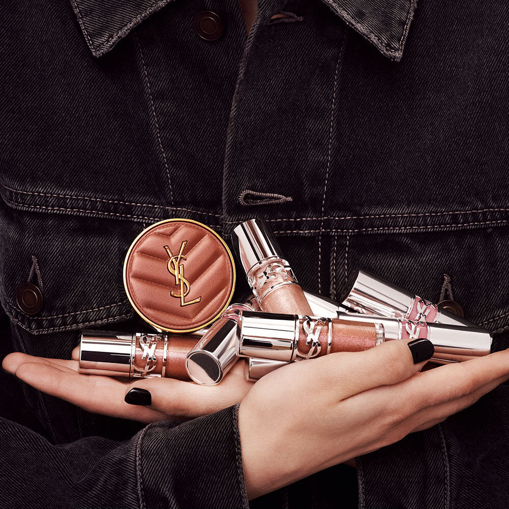 Hands holding YSL LOVESHINE Plumping Lip Oil Gloss and Make Me Blush, showcasing luxury beauty products.