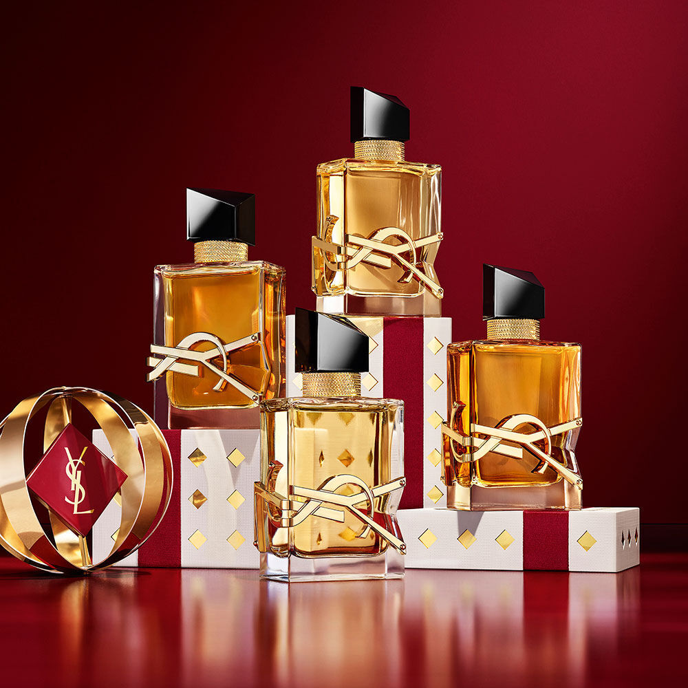Frascos de la fragancia YSL LIBRE superpuestos sobre un lujoso estuche dorado con motivos navidenos.