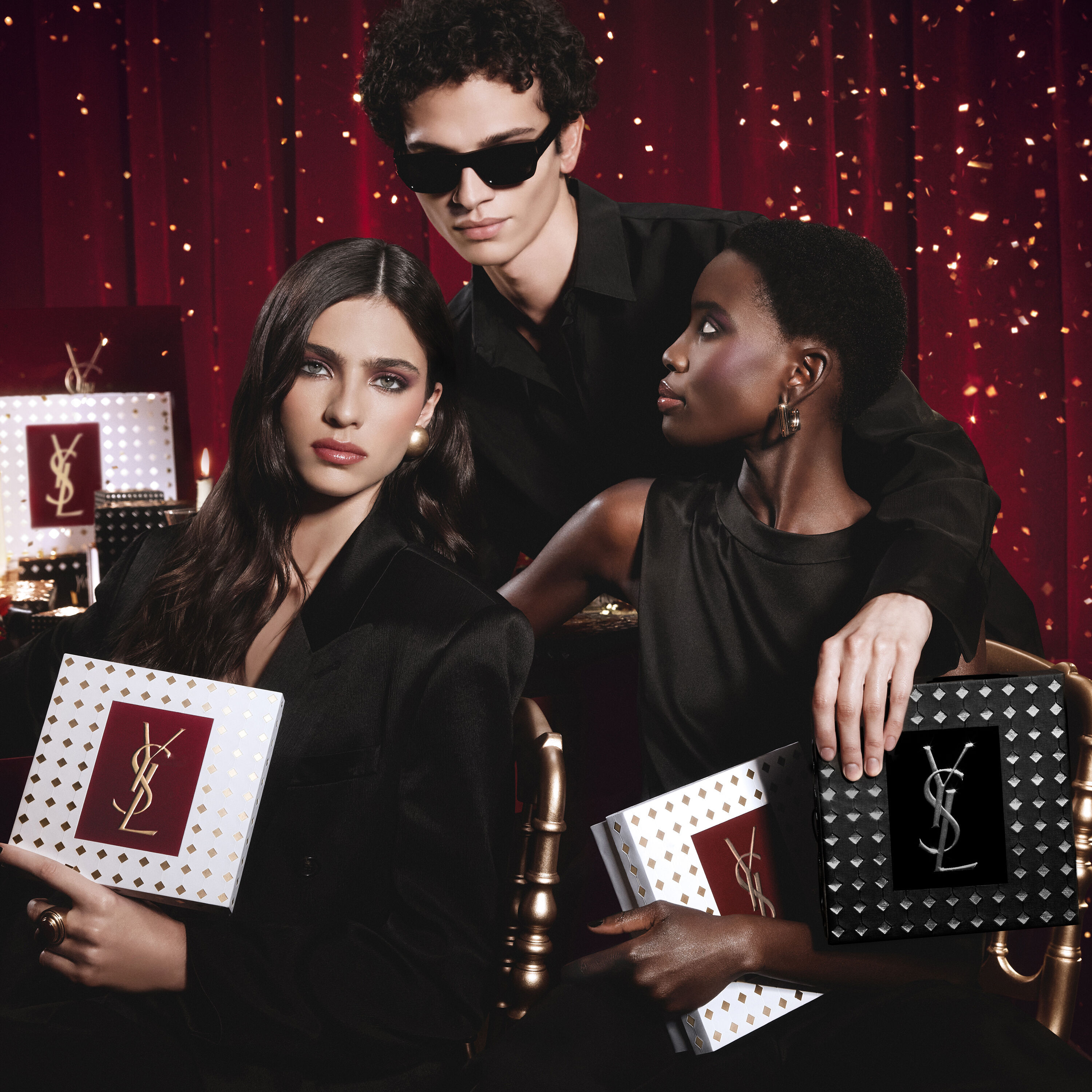 Modelos posando juntas con lujosas cajas de regalo navidenas de YSL en un ambiente festivo.