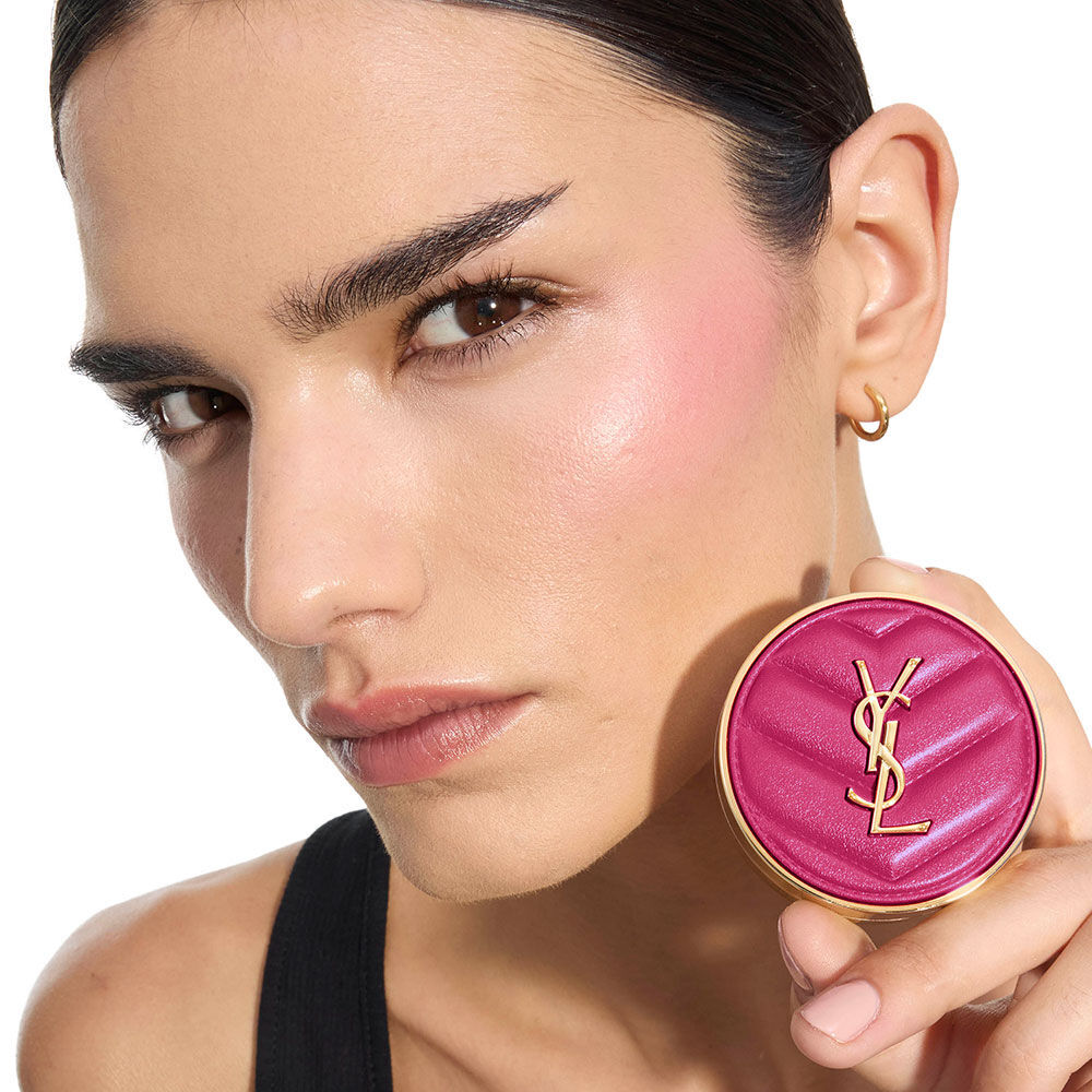 Iman, medium skin, holding a fuchsia YSL Make Me Blush Powder Blush in shade 66, showcasing vibrant blush on her cheek.