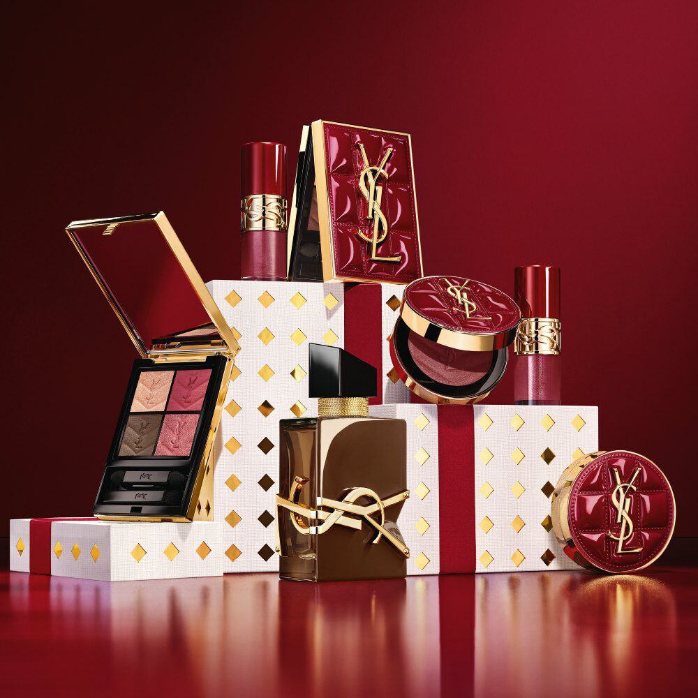 Coleccion de maquillaje y cofre de fragancias YSL Navidad 2026 sobre pedestales blancos con puntos dorados en burdeos.