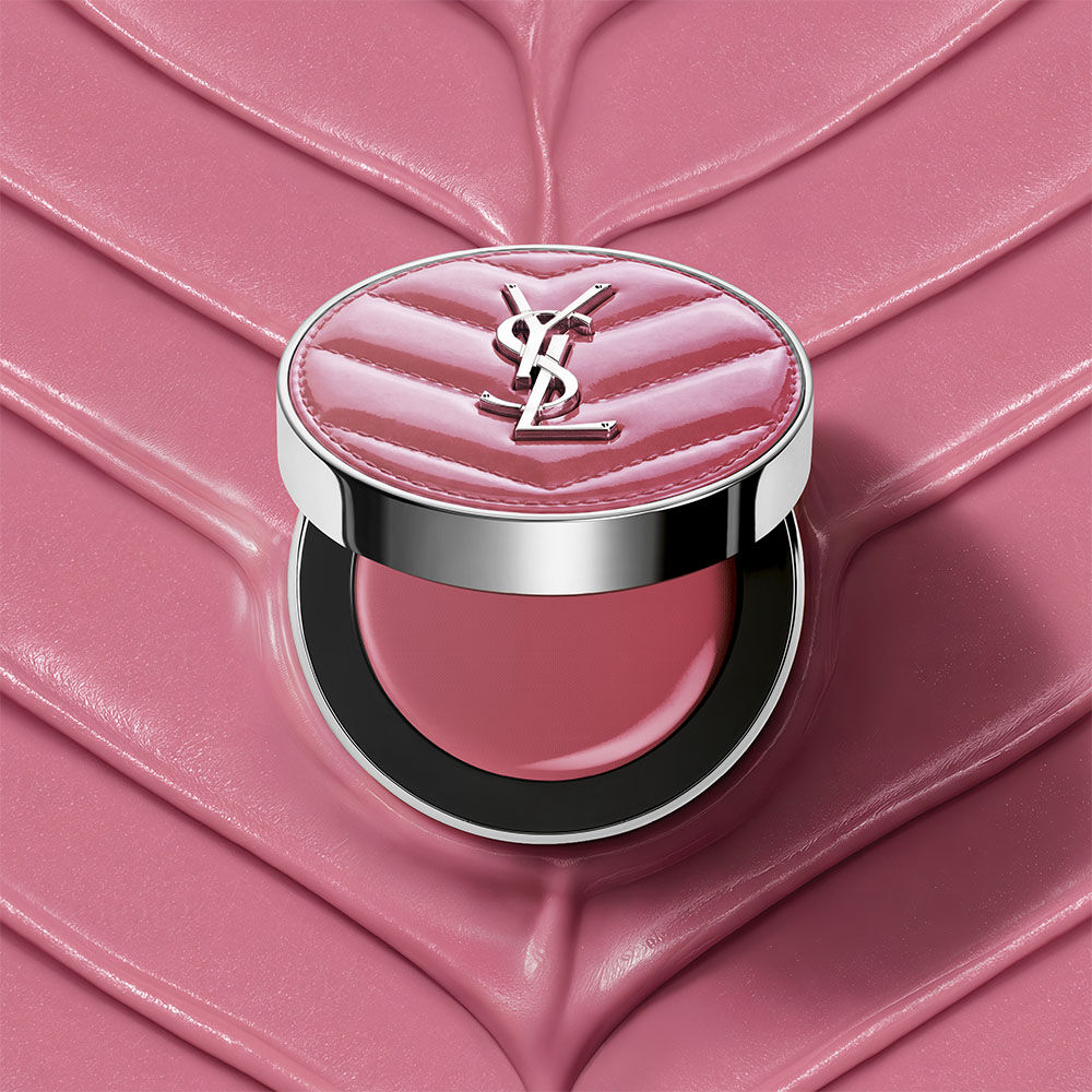 Una polvera abierta de YSL Make Me Blush Lifted Glow Cream Blush en el tono #44 Nude Lavalliere sobre un fondo crema texturizado en rosa a juego.