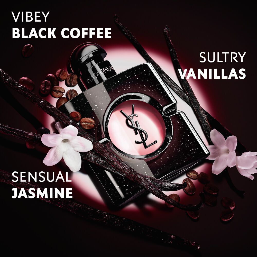 Primer plano de granos de cafe tostados, vainas de vainilla y flores de jazmin dispuestos sobre el iconico frasco de Black Opium Eau de Parfum con la Cassandre de YSL.